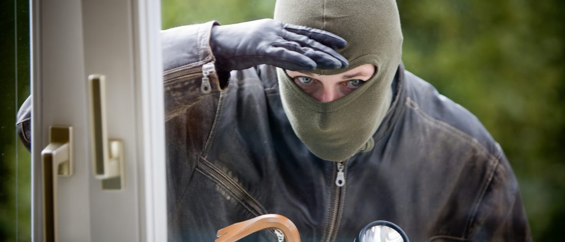 Cambrioleur qui inspecte l'intérieur d'une maison avec un pied de biche et une lampe torche